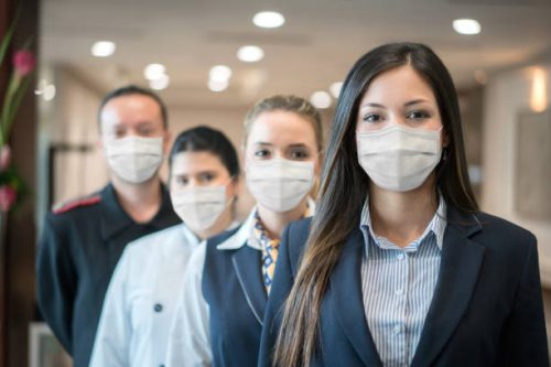 Group of Latin American hotel workers in a row wearing facemask during the COVID-19 pandemic and looking at the camera